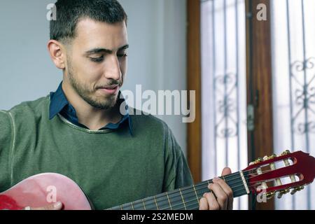Jeune homme assis à l'intérieur jouant une guitare acoustique rouge. Banque D'Images