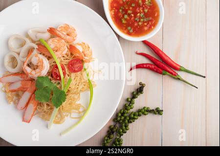 Nouilles instantanées sautées avec crevettes et bâtonnets de crabe avec tomates et poivrons dans une assiette blanche sur un plancher en bois. Banque D'Images