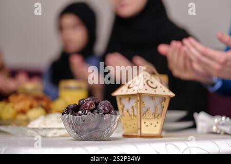Heureuse famille musulmane ensemble faisant iftar dua pour faire la pause jeûne pendant le Ramadan à la table à manger à la maison se concentrer sur un bol de dates. Banque D'Images