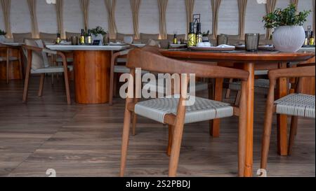 Un élégant restaurant intérieur avec chaises en bois et tables rondes, au décor moderne, à l'éclairage tamisé et à l'atmosphère chaleureuse. Banque D'Images