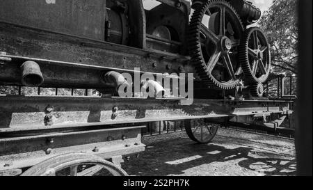 Gros plan noir et blanc d'une ancienne machine industrielle avec de gros engrenages et tuyaux métalliques, montés sur roues, mettant en valeur l'ingénierie historique Banque D'Images