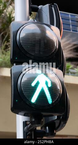 Gros plan d'un feu de circulation pour piétons affichant une figure de marche verte, indiquant qu'il est sûr de traverser, avec un fond urbain. Banque D'Images