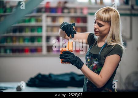 Portrait d'une technicienne graphique professionnelle féminine debout à l'atelier d'impression avec la boîte d'encre dans les mains et le mélangeant. Souriant atelier d'impression expérimenté Wor Banque D'Images