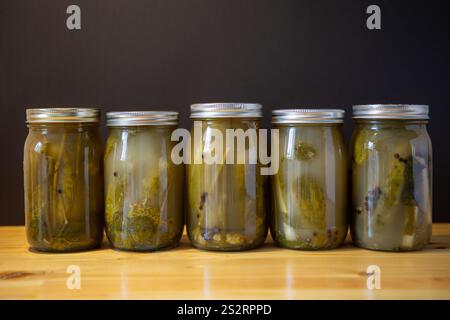 Pots en verre remplis de concombres marinés sur une table en bois sur un fond sombre. Banque D'Images