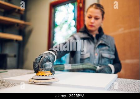 Travailleuse utilisant une ponceuse électrique dans un atelier spacieux. Femme charpentier ponçant le bois et construisant des meubles faits à la main. Concentrez-vous sur une ponceuse électrique. Banque D'Images