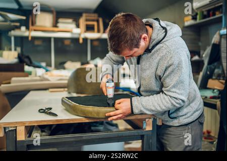 Un artisan concentré rembourse un siège de chaise à l'atelier de meubles. Un artisan rembourre des meubles faits à la main dans son atelier. Banque D'Images