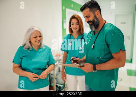 Trois professionnels de la santé, deux femmes et un homme, se tiennent debout dans un couloir d'hôpital et discutent des dossiers des patients, mettant en valeur le travail d'équipe et la voiture de santé Banque D'Images