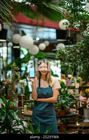 Fleuriste montrant un smartphone entouré de fleurs et de plantes dans un fleuriste Banque D'Images