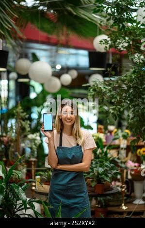 Fleuriste montrant un smartphone entouré de fleurs et de plantes dans un fleuriste Banque D'Images