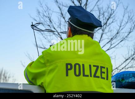 08 janvier 2025, Brandebourg, Francfort (Oder) : un policier se tient devant le drapeau de deuil sur l'antenne de son véhicule de police au quartier général de la police est. Le drapeau de deuil symbolise la sympathie des collègues pour la mort d'un policier de Saxe. Un policier de Dresde a été capturé et tué le 7 janvier 2025 à Lauchhammer dans le Brandebourg lors d'une chasse à l'homme pour des voleurs de voitures. Photo : Patrick Pleul/dpa Banque D'Images