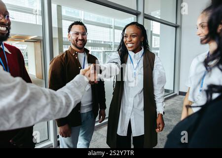 Jeune femme d'affaires serrant la main à un collègue dans un cadre de bureau, entourée de collègues souriants. Banque D'Images