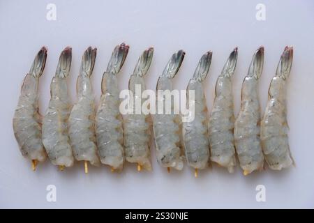 Gros plan de crevettes fraîches pelées non cuites sur une planche à découper blanche. Banque D'Images