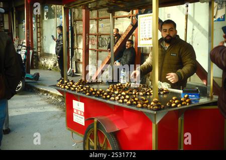 Istanbul, Turkiye - 30 novembre 2024 : un vendeur de nourriture de rue vend des châtaignes grillées à l'aide d'un chariot turc rouge traditionnel Banque D'Images