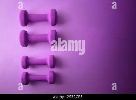 Ensemble de deux paires d'haltères violets en néoprène isolés sur fond violet. Vue de dessus. Banque D'Images