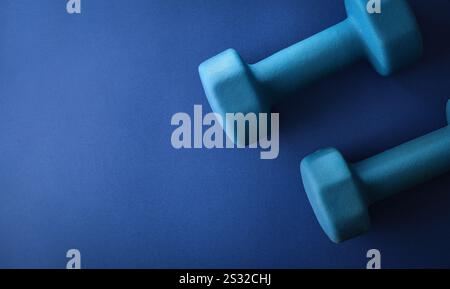 Fond avec deux haltères octogonaux en néoprène bleu isolés sur un fond bleu. Vue de dessus. Banque D'Images