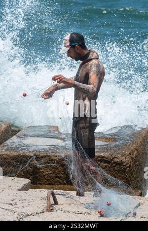 Alexandrie, Égypte. 26 juin 2024. Un jeune pêcheur égyptien portant une combinaison de plongée dispose son filet sur le front de mer Méditerranée d'Alexandrie, deuxième Banque D'Images
