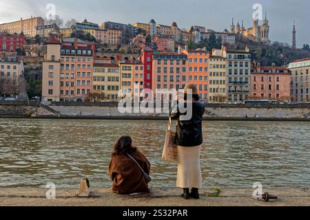 LYON, 17 décembre 2024 : touristes sur les rives de la Saône avec le vieux quartier du patrimoine mondial et la basilique de Fourvière en arrière-plan. Banque D'Images
