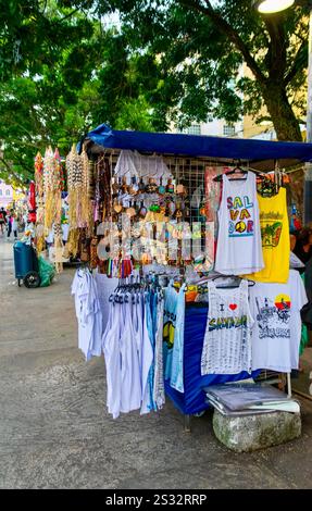 Stand souvenir dans Pelourinho 'Praça da Sé', place avec de l'artisanat et des T-shirts à l'ombre des arbres tropicaux. La culture de rue de Salvador est exposée. Banque D'Images