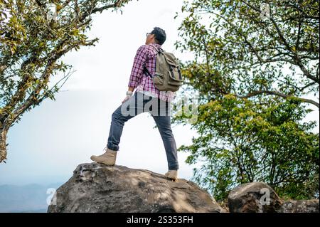 Vue arrière du jeune homme de randonnée asiatique avec sac à dos debout et regardant vers avec heureux sur le sommet de la montagne rocheuse, espace de copie Banque D'Images