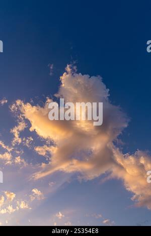 La lumière du soleil tôt le matin filtre à travers les nuages, créant une touche de couleur contre un ciel bleu. Banque D'Images