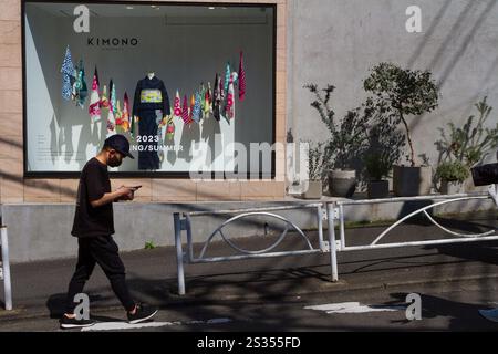 Un jeune japonais, utilisant un téléphone intelligent, passe devant un magasin avec un kimono dans la vitrine. Harajuku, Tokyo, Japon. Banque D'Images