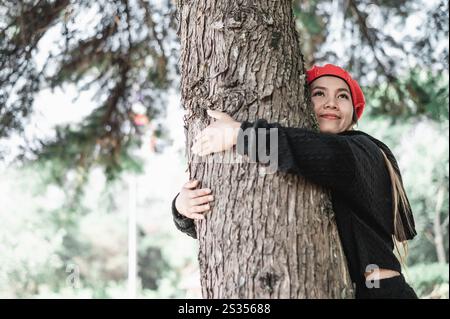 Jeune femme satisfaite embrassant un grand arbre avec une expression heureuse avec espace de copie. Concept de soins pour l'environnement. Banque D'Images