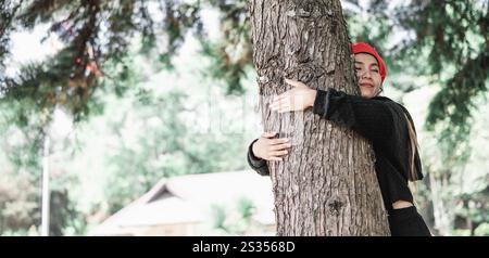 Jeune femme satisfaite embrassant un grand arbre avec une expression heureuse avec espace de copie. Concept de soins pour l'environnement. Banque D'Images