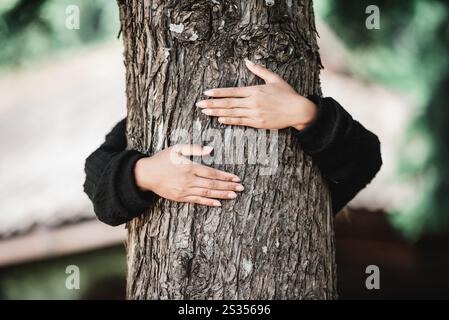 Jeune femme satisfaite embrassant un grand arbre avec une expression heureuse. Concept de soins pour l'environnement. Banque D'Images