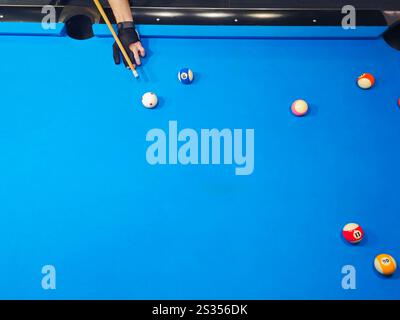 Queue de billard dans les mains du joueur masculin frappant la balle blanche pendant la vue de dessus du jeu. Banque D'Images