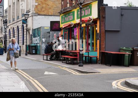 Cardiff Wales - 7 août 2024 ; les gens dînent devant le bar à tacos coloré de Quay Street tandis qu'une femme passe devant. Banque D'Images