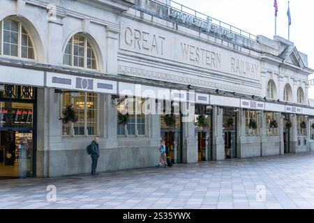 Cardiff Wales - 6 août 2024 ; devant la gare où un homme attend et où le mouvement de la femme s'estompe alors qu'elle marche en tirant une valise. Banque D'Images