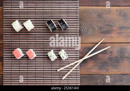 Rouleaux de sushi et baguettes en bois se situent sur une paille de bambou serwing mat. Cuisine asiatique traditionnelle. Vue d'en haut. Banque D'Images