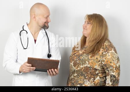 Une femme aux longs cheveux blonds portant une blouse à motifs a une conversation avec un médecin masculin vêtu d'un manteau blanc. T Banque D'Images