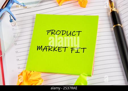 Une note autocollante vert vif affiche les mots Product market FIT sur un carnet ligné. Des papiers brouillés entourent la note, suggérant un brainstorming et Banque D'Images
