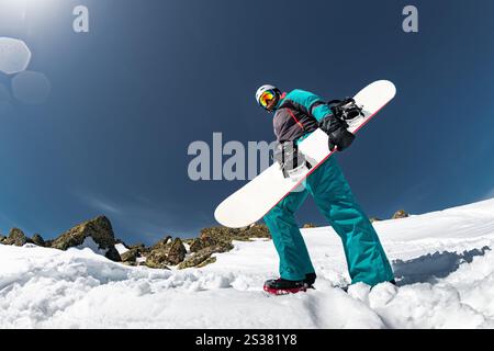 Vue d'angle drôle inhabituelle au snowboarder est debout contre la neige et le ciel bleu. Vue de dessous Banque D'Images