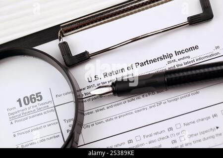 IRS Form 1065 US Return of Partnership Income blanc sur la tablette A4 repose sur la table de bureau avec stylo et loupe en gros plan Banque D'Images