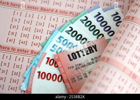 Billet de loterie rouge se trouve sur des feuilles de jeu roses avec des factures d'argent rupiah indonésiennes. Concept de jeu de loterie ou dépendance au jeu en indonésie. Rouge Banque D'Images