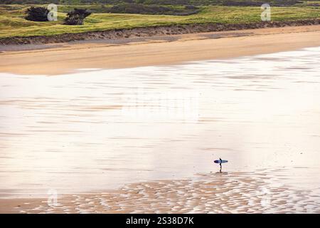Surfeur marchant sur une plage de sable et portant sa planche de surf un jour d'été Banque D'Images