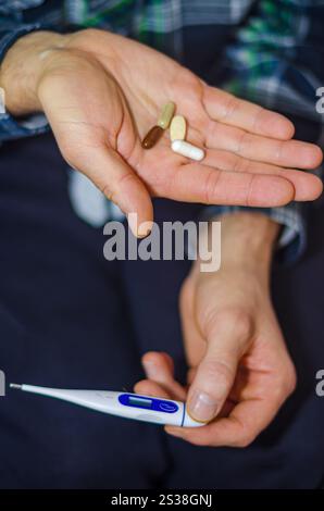 Gros plan des mains d'une personne tenant un thermomètre numérique et diverses pilules. Photo de haute qualité Banque D'Images