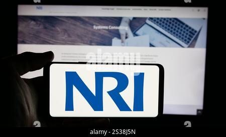 Dans cette illustration photo, une personne tient un téléphone portable avec le logo de la société Nomura Research Institute Ltd. (NRI) sur l'écran devant la page Web. Banque D'Images