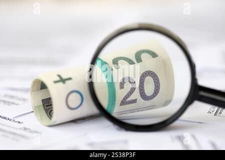 L'argent zloty polonais et la loupe sur une grande quantité de formulaires fiscaux polonais se rapprochent. Comptabilité, bureaucratie et routine des contribuables en Pologne. Polonais Banque D'Images