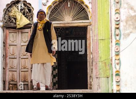 Homme en tenue traditionnelle assis à l'extérieur contre un mur altéré dans un cadre de village indien Banque D'Images