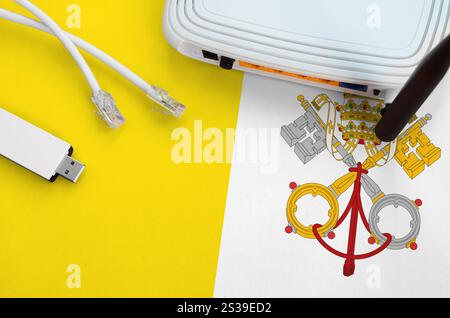 Drapeau de l'État de la Cité du Vatican représenté sur la table avec câble Internet rj45, adaptateur wi-fi usb sans fil et routeur. Concept de connexion Internet. Cité du Vatican Banque D'Images