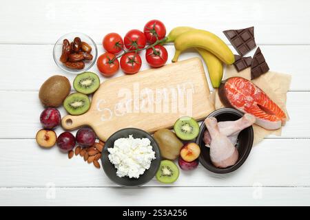 Planche en bois avec le mot sérotonine et différents produits frais sur table blanche, pose à plat Banque D'Images