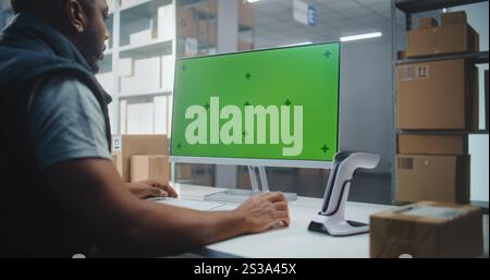 Service de livraison : African American Warehouse Associate scanne le code sur la boîte en carton avec scanner, entre les informations sur le colis sur ordinateur. L'écran de l'ordinateur affiche la maquette de la touche Chroma de l'écran vert. Portable. Banque D'Images