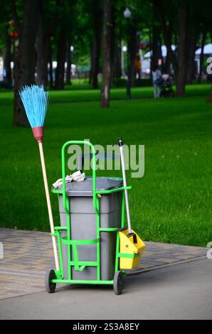 Chariot de service de nettoyage plein de fournitures et d'équipement avec poubelle grise pour un nettoyant professionnel contre l'herbe verte dans le parc public. Nettoyage Banque D'Images