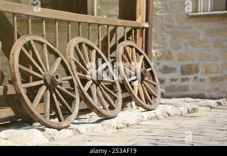 Trois vieilles roues en bois pour charrettes à chevaux appuyées contre un mur en bois en perspective Banque D'Images