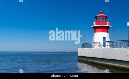 Un phare rouge et blanc se dresse fièrement au sommet d'une jetée robuste, surplombant l'eau environnante. Banque D'Images