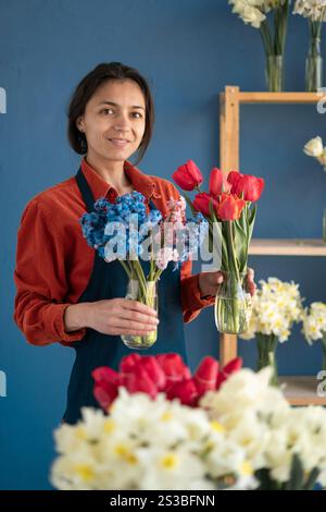 Propriétaire de petite entreprise fleuriste tenant des bouquets de tulipes et jacinthes debout dans son magasin de fleurs. Livraison de fleurs Banque D'Images