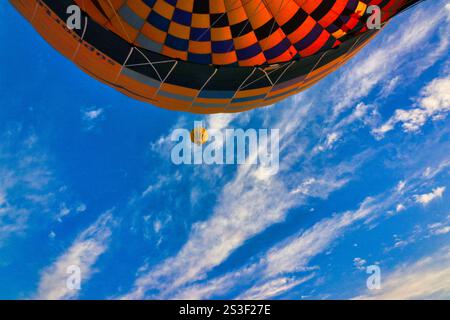 Une montgolfière monte dans un ciel bleu strié de nuages emmenant des touristes au-dessus du désert du Sahara à Louxor, en Égypte Banque D'Images